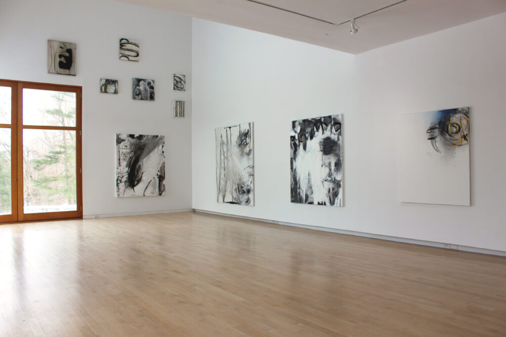 Gallery with a window in the left corner with abstract paintings on the walls.