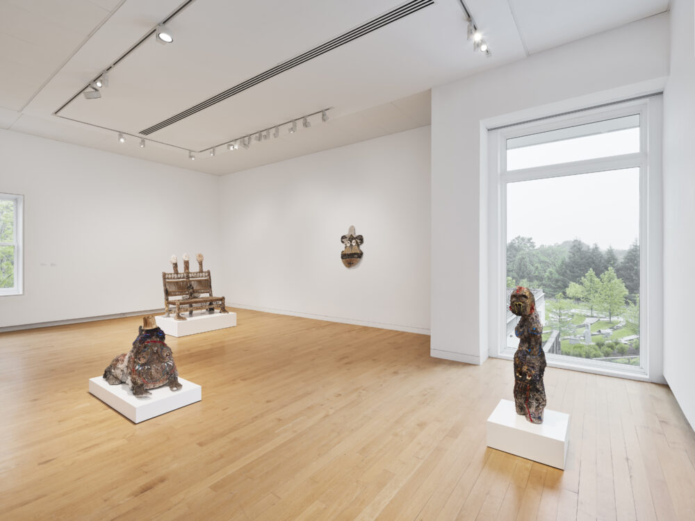 Sculptures in cream, brown, neutral, and green tones in a museum gallery with white walls and wooden floors.