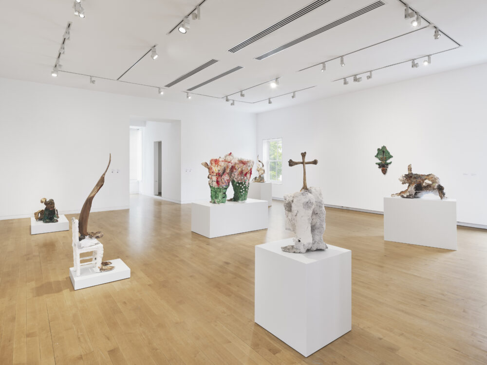 Sculptures in cream, brown, neutral, and green tones in a museum gallery with white walls and wooden floors.