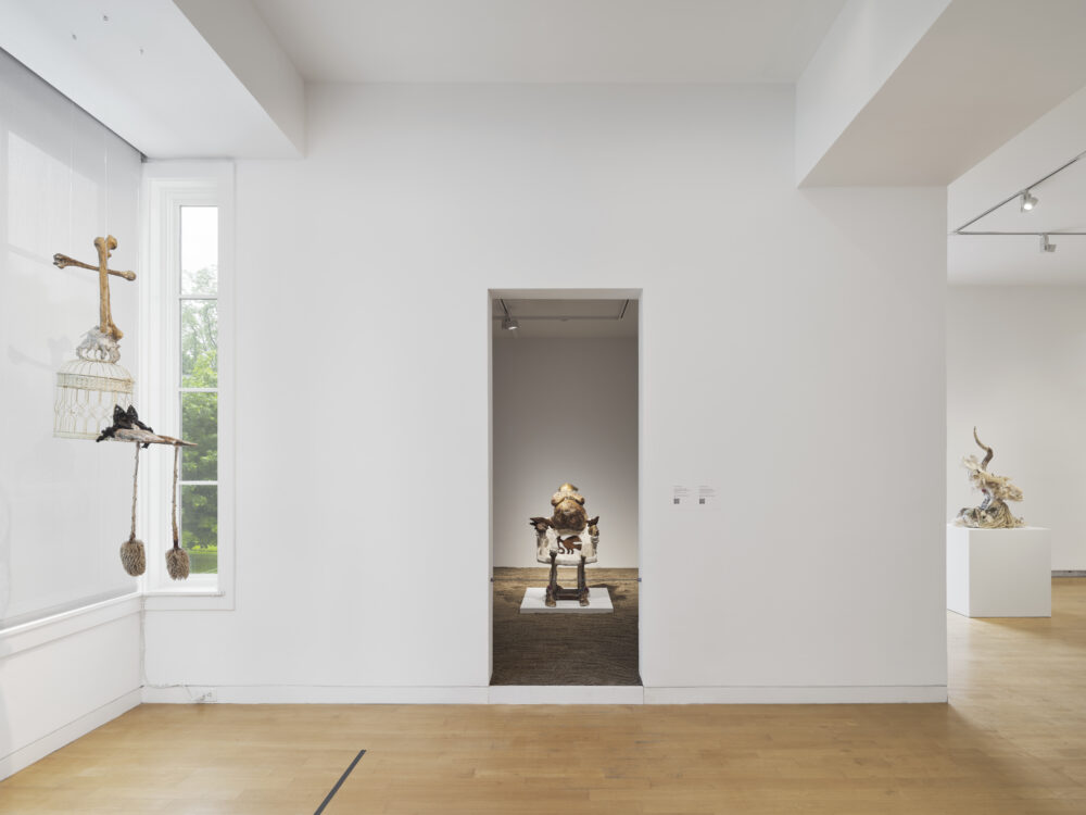 Sculptures in cream, brown, neutral, and green tones in a museum gallery with white walls and wooden floors.
