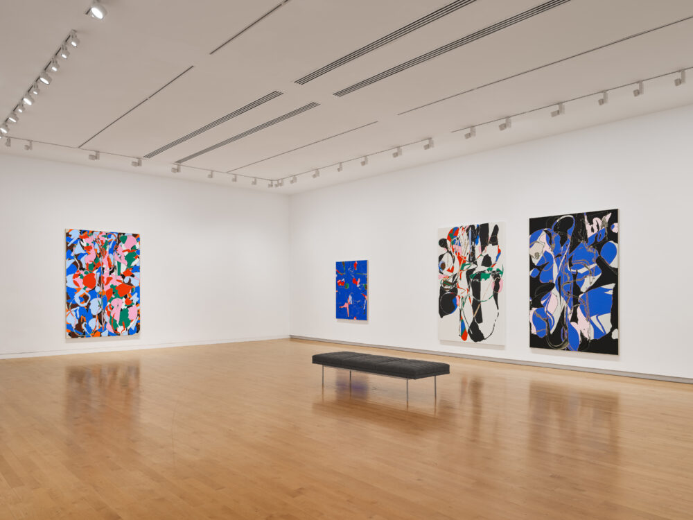Three abstract paintings on a museum wall. The paintings are multi-colored—mostly red, blue, black, and white. There is a bench on the floor.