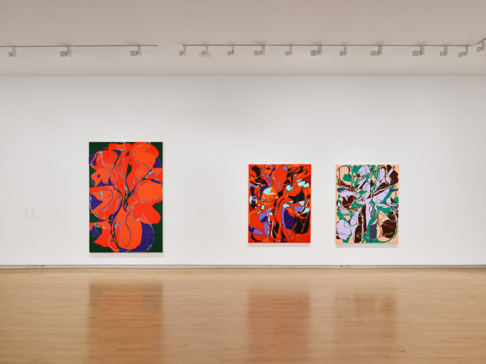 Three abstract paintings in a museum. One is large and mostly red-orange; the other two are smaller.