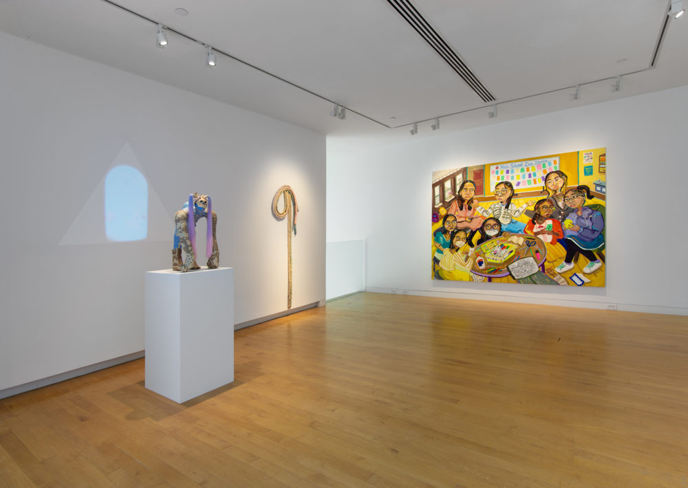 Gallery with a figurative painting in the background, an abstract soft textile work mounted on the wall and a anthropomorphic figurative sculpture with a video