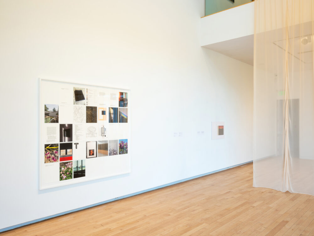 Framed photographs and other collected imagery in the format of a calendar framed on the wall next to a tall site-specific nude curtain.