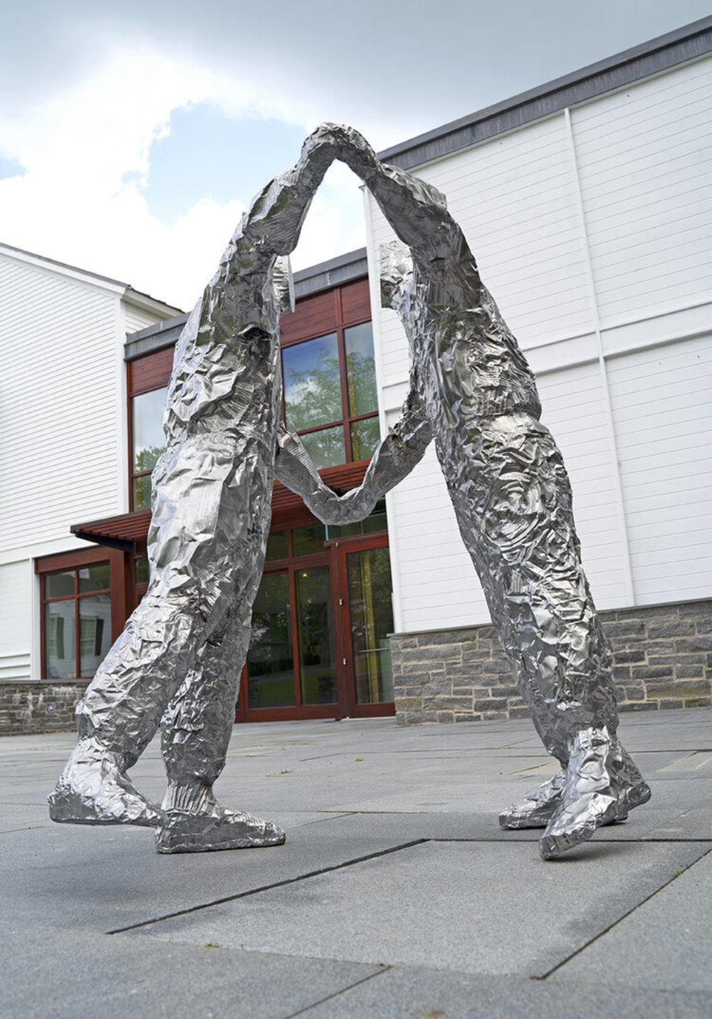 Two figures made out of crumpled baking pans cast in polished stainless steel with a large white building in the background