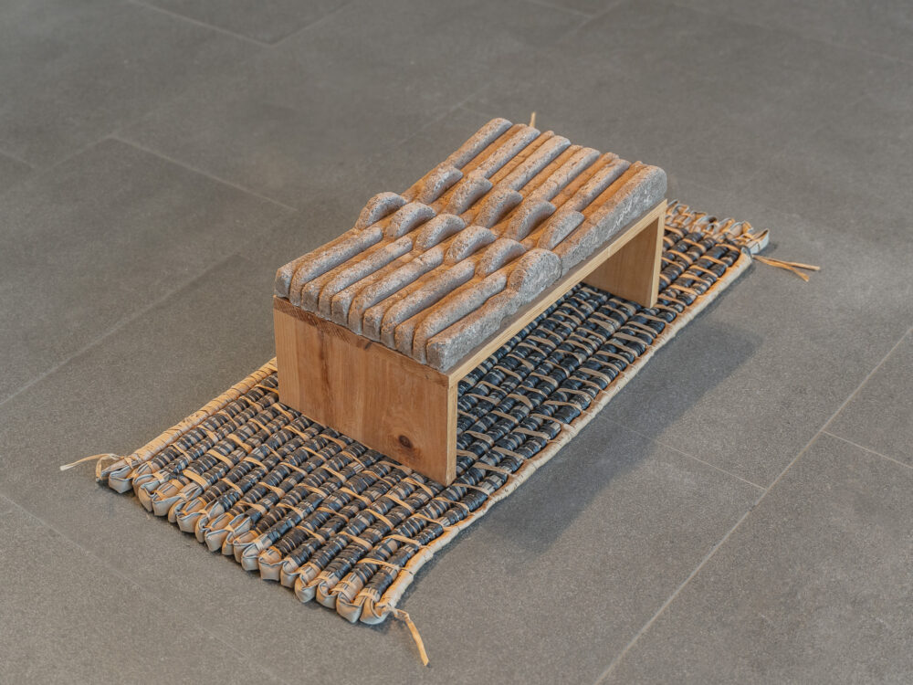 A small adobe structural sculpture atop of a textile work