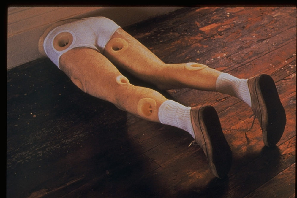 a pair of men's legs protruding from the wall with white underwear, shoes and socks with drains spotted all over the legs