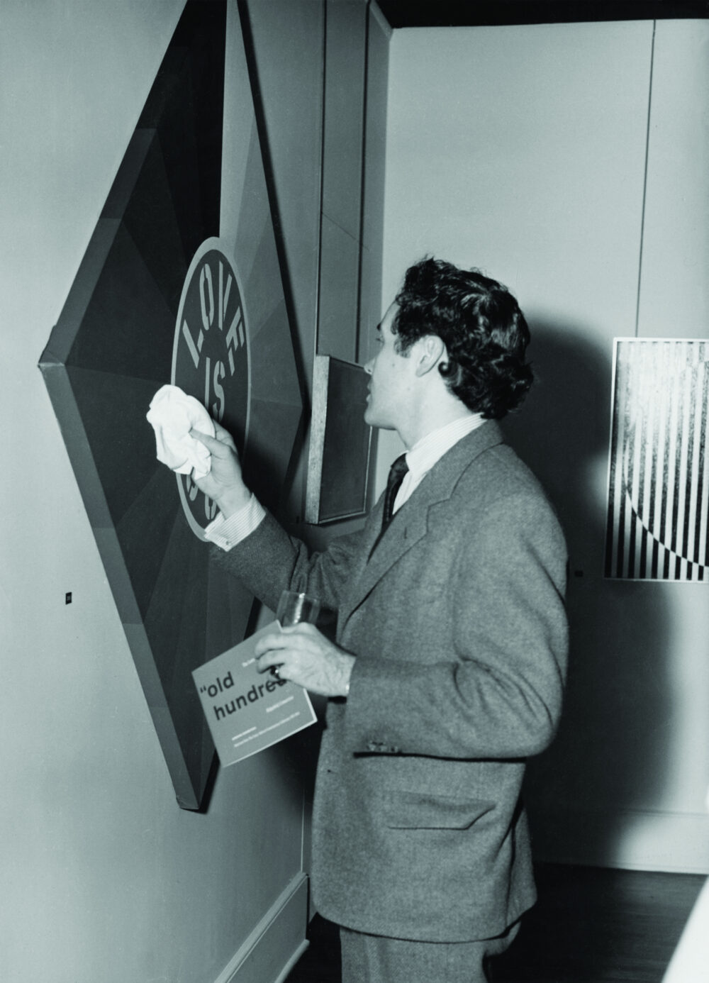Robert Indiana cleaning his painting Love Is God with his handkerchief before exhibition opening.