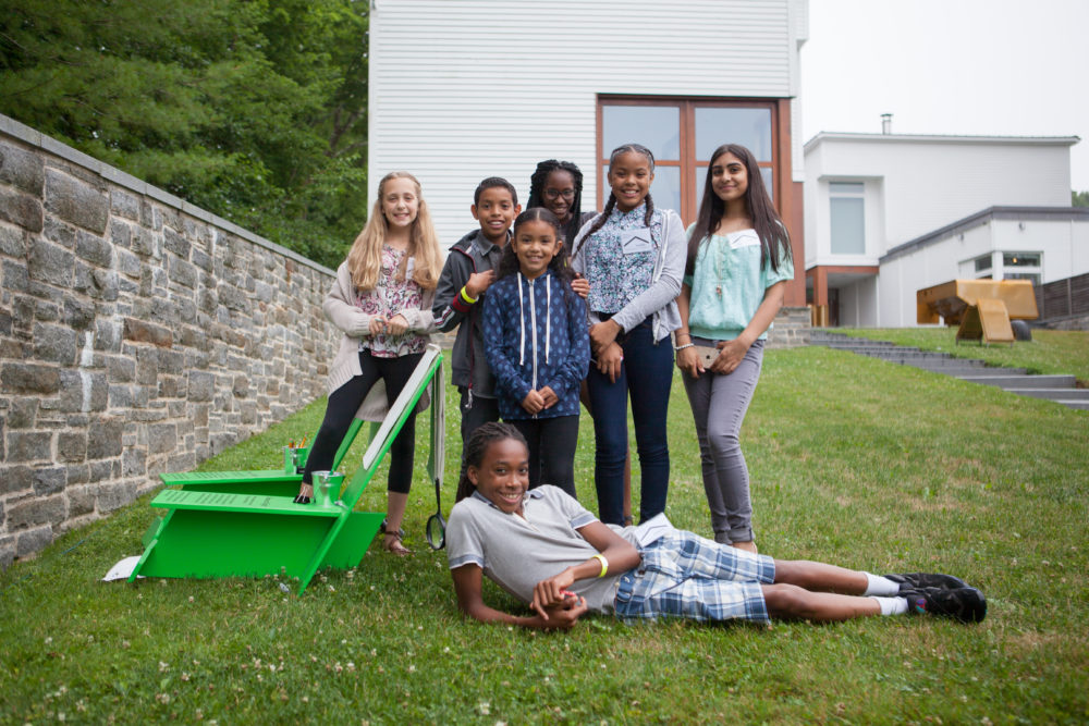 A group of students in the Museum's Sculpture Garden by a green lawn chair.