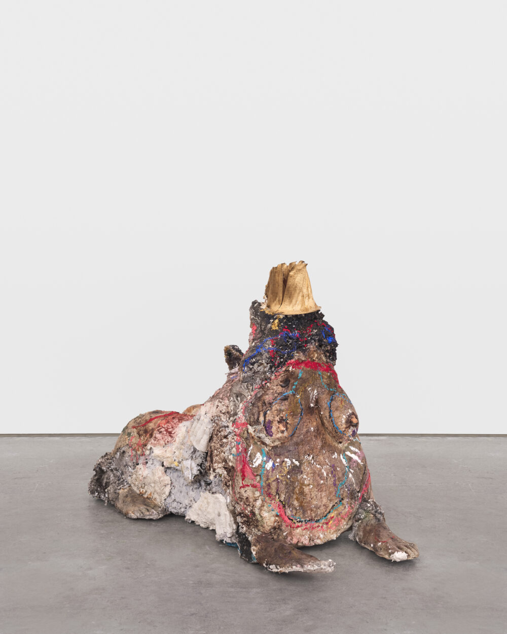 A gold and brown sculpture of a creature that has a human pregnant torso and four feet on the ground like a sphynx.