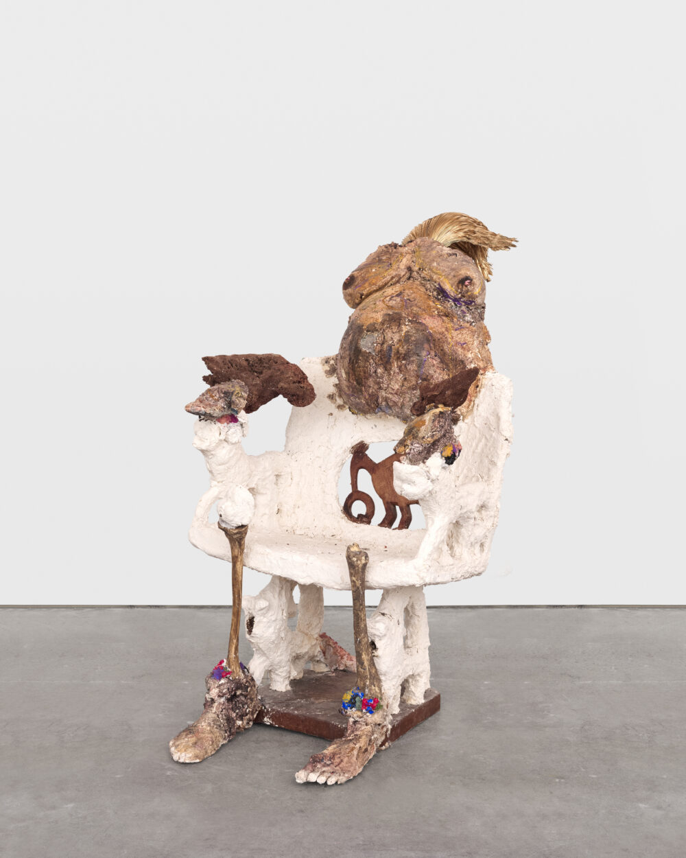 Brown and white sculptural artwork of an abstract chair with a pregnant torso, bones, and feet.