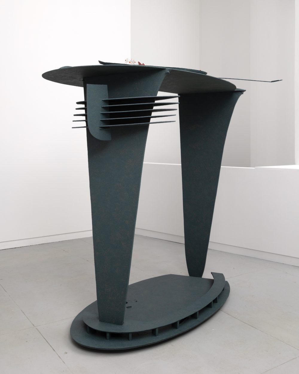 Dark gray sculpture with two legs and an oval base with a flat looking top.