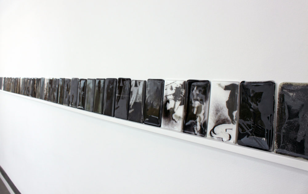 A row of black and white etched glass tiles on a shelf on a white wall.