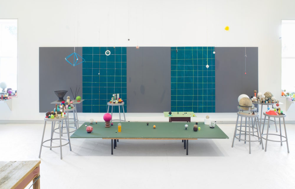 Small, circular objects sitting on stools. Green table in center of the room with small, circular objects.