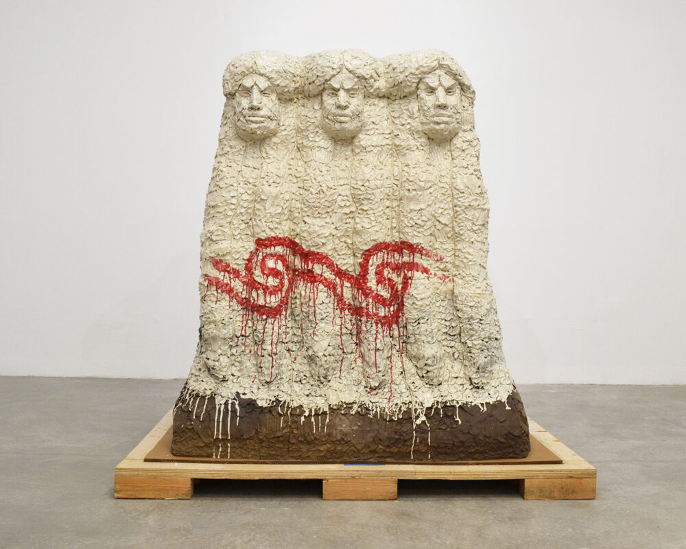 Large white ceramic sculpture of three interconnected women with a red marking on the front.