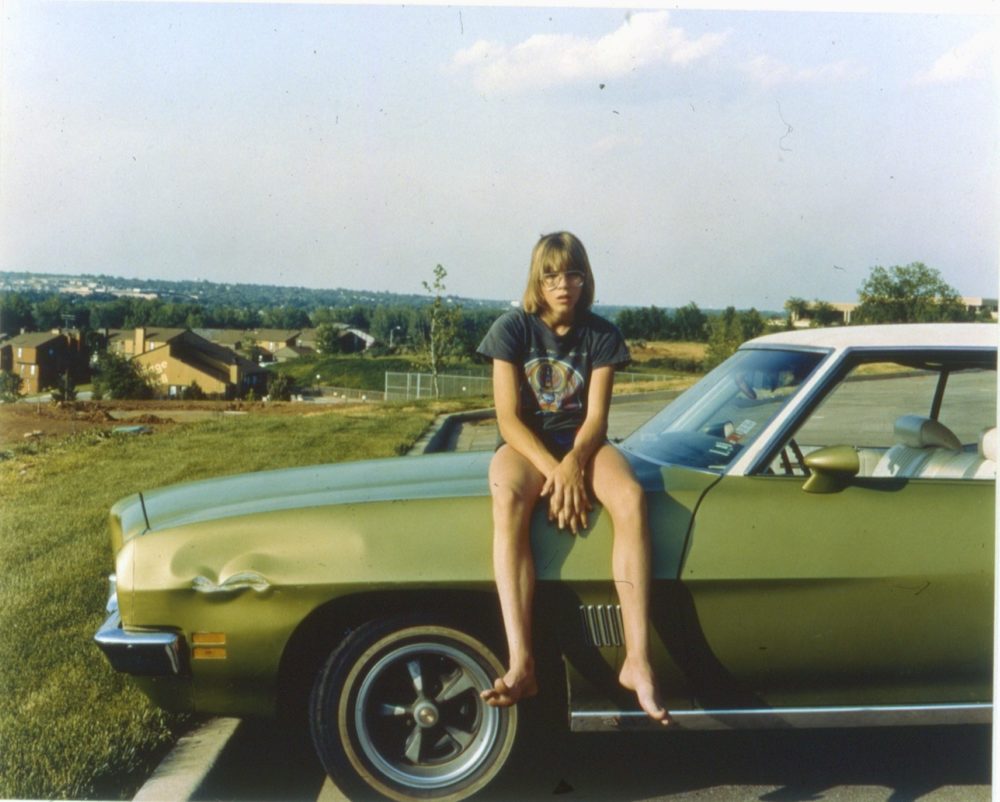This is a photograph of a young boy sitting on a green car in a field