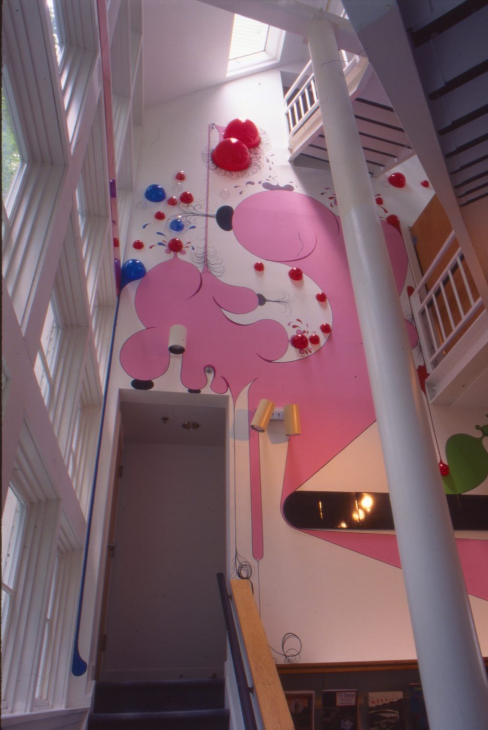 This is a photograph from the Pop Surrealism exhibition which features a large pink, surrealist mural by Paul Henry Ramirez