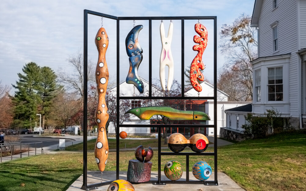 A large-scale sculpture made from steel and salvaged tree matter containing hand-carved, brightly painted objects resembling fishing lures.