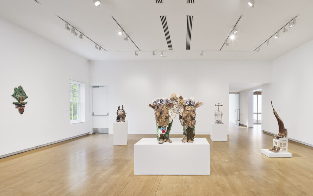 Sculptures in cream, brown, neutral, and green tones in a museum gallery with white walls and wooden floors.