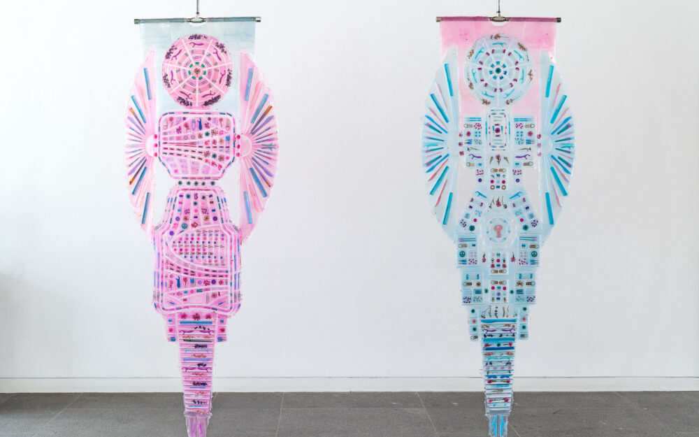 Two hanging transparent sculptures with small objects embedded within.