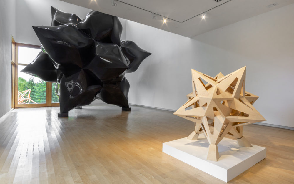 Smaller wooden star sculpture in foreground, large-scale black star sculpture in background.