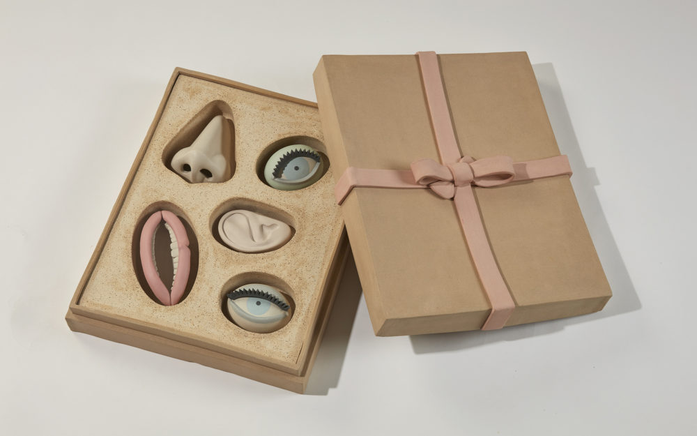 A gift box with small, sculptural works of a nose, two eyes, an ear, and a mouth