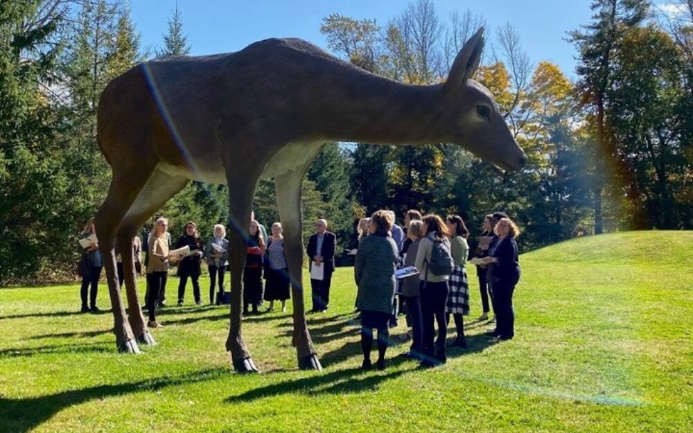 Group of people standing around a large scale sculpture of a white tailed deer in the Sculpture Garden.
