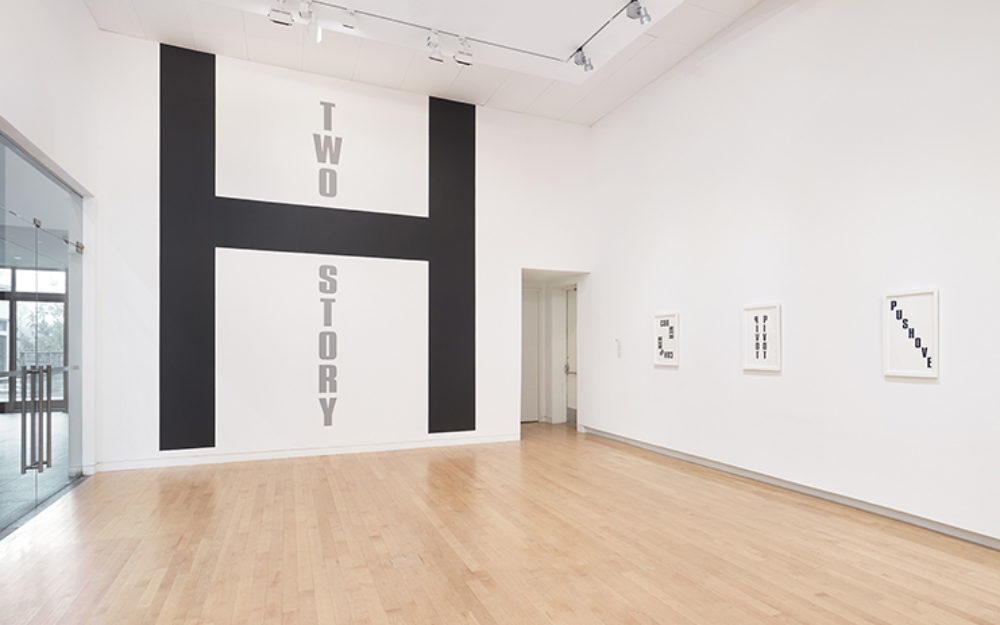 Large black H on gallery wall with the words "Two Story," in gray