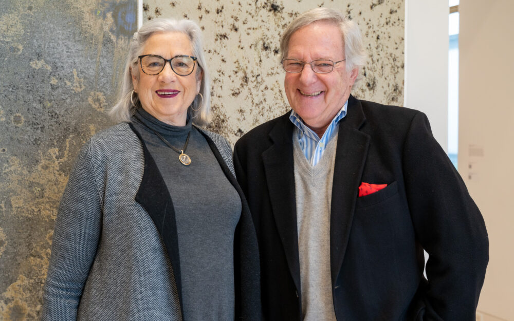 A man and woman smiling in front of an artwork