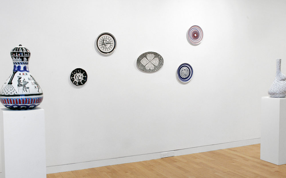 Ceramic vases sit on white pillars, ceramic plates hang on gallery walls