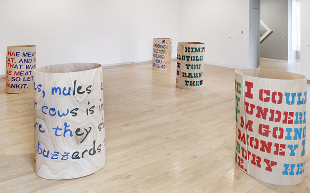 Five circular forms with lettering on them sit on the gallery floor