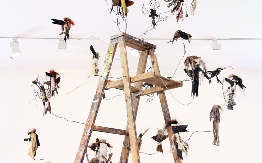 Small figurative sculptures surrounding the top of a wooden ladder