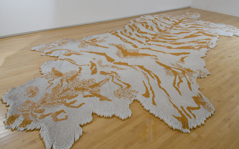 Cigarettes arranged to resemble a tiger skin rug on a wooden floor.