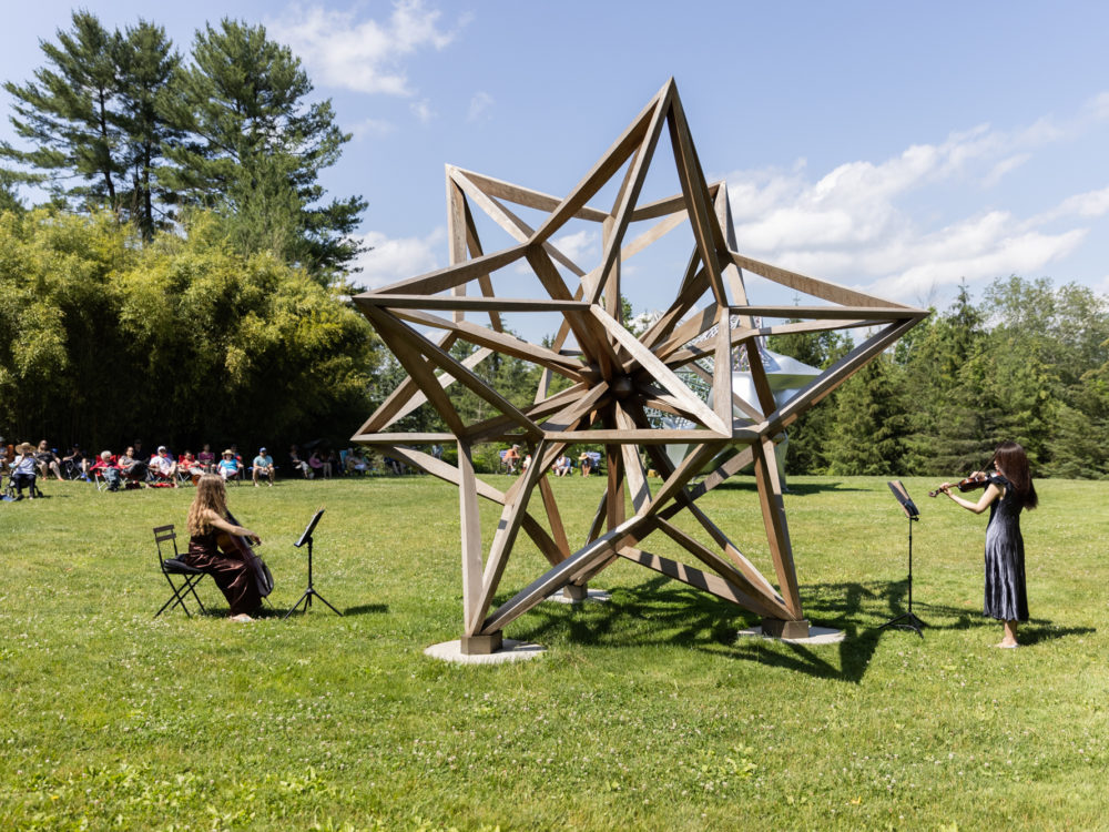 Two musicians perform in front of a large wooden star sculpture