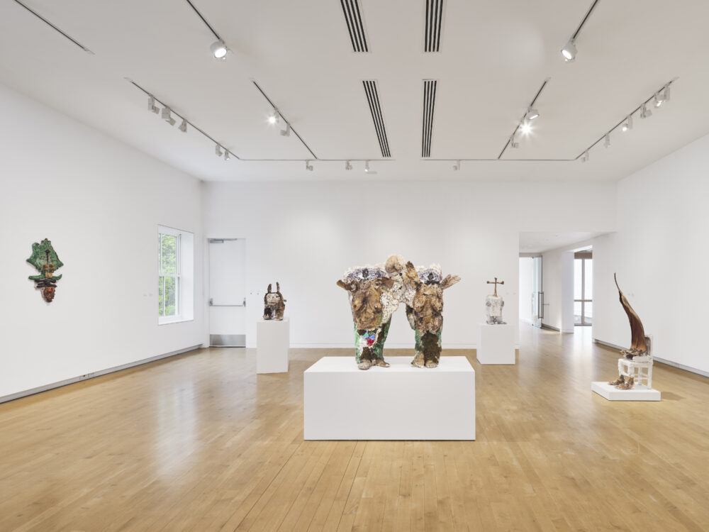 Sculptures in cream, brown, neutral, and green tones in a museum gallery with white walls and wooden floors.