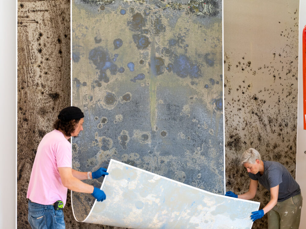 Art handlers siting paper scroll work suspended from ceiling.