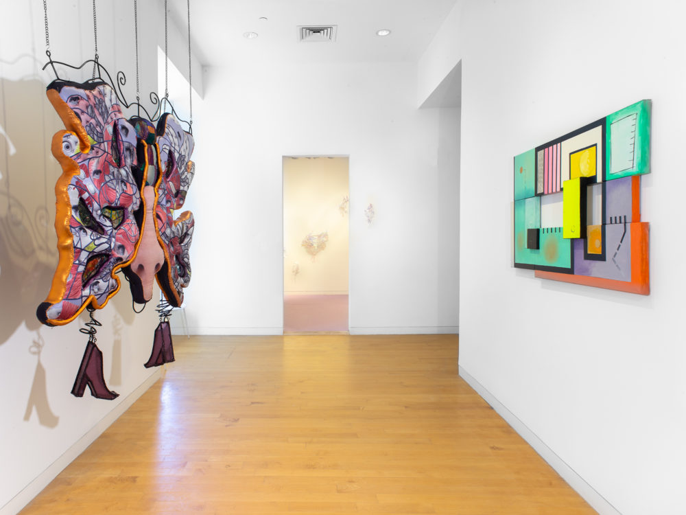 Gallery with a hanging sculpture on the left and a painting the right and an installation in the background at center.