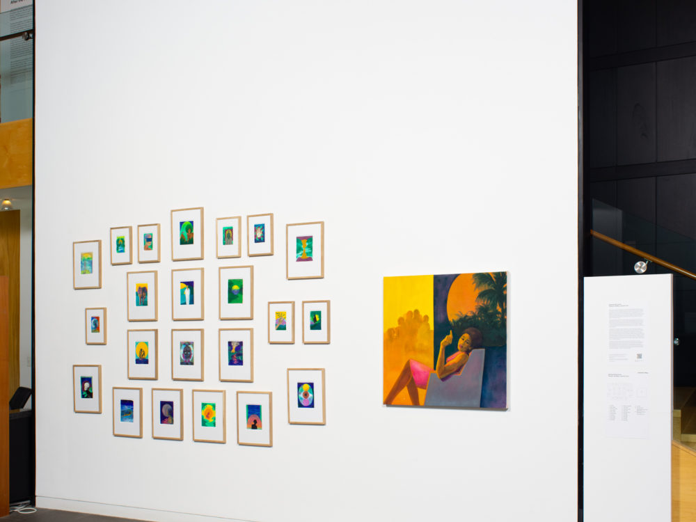 Installation of small watercolor paintings hung salon style with a larger painted canvas hung to the right.