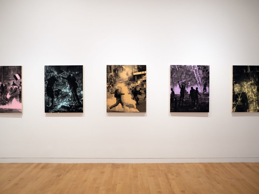 White wall with five black and single color drawings of protests.