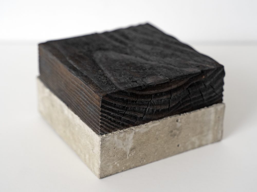 A small square of concrete with a square of the same size of burnt wood attached.