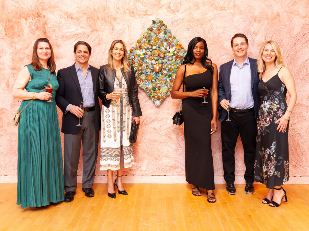 Guests standing in Layo Bright's gallery with one of her floral glass works on the wall at the center.