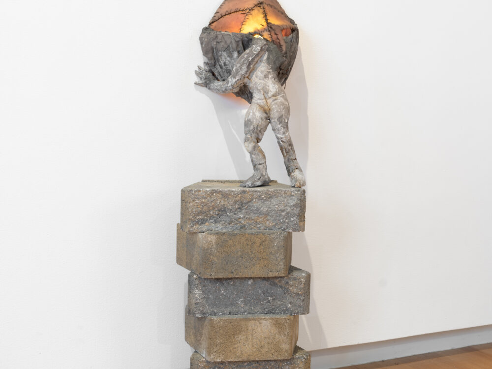 A small scale figurative sculpture installed against a wall.