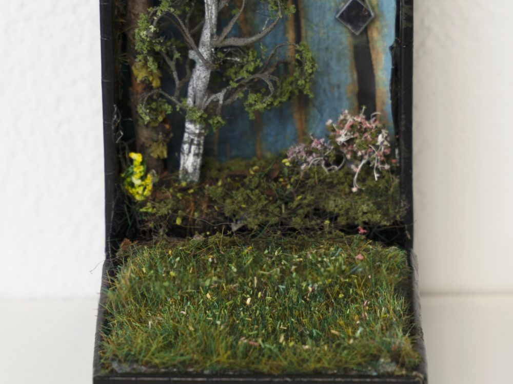 Open small jewelry box with a landscape diorama inside including grass and trees.