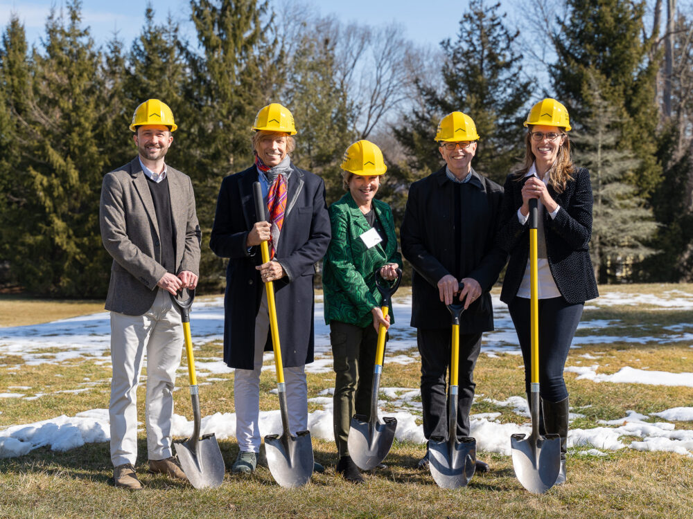 People wearing yellow hard hats and holding shovels outside.