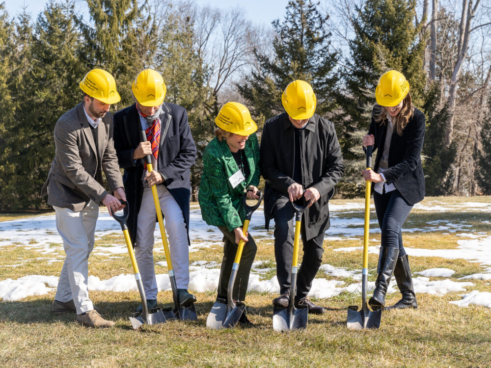 People digging in the ground wearing yellow hard hats.