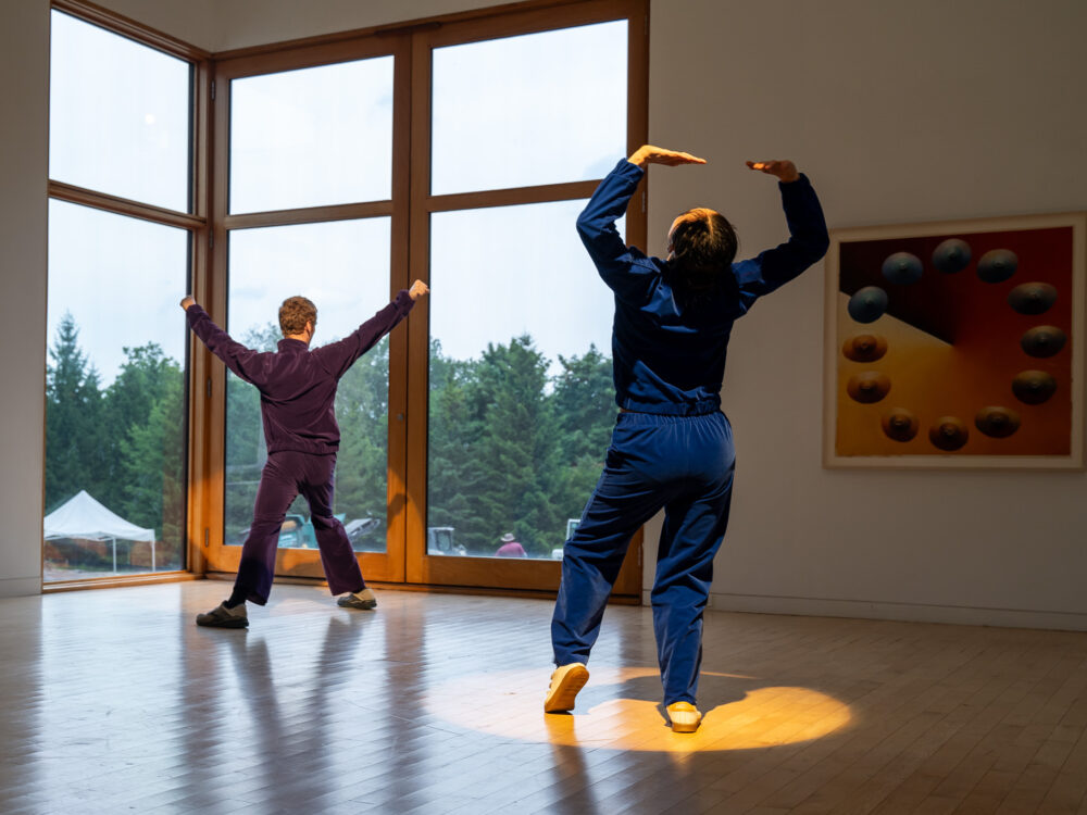 Two dancers in blue and purple velour jumpsuits performing in an art gallery