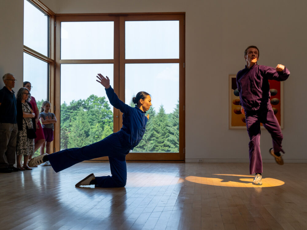 Two dancers in blue and purple velour jumpsuits performing in an art gallery