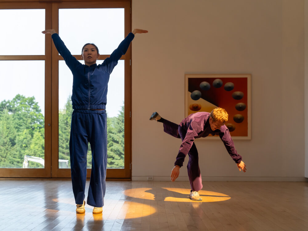 Two dancers in blue and purple velour jumpsuits performing in an art gallery