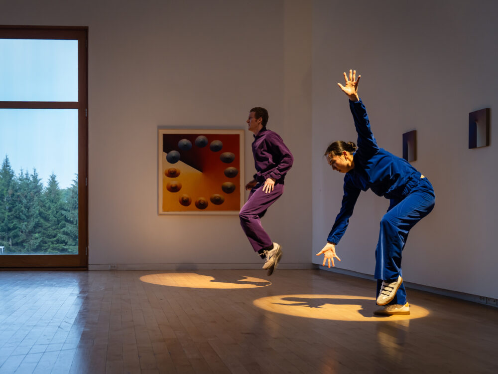 Two dancers in blue and purple velour jumpsuits performing in an art gallery