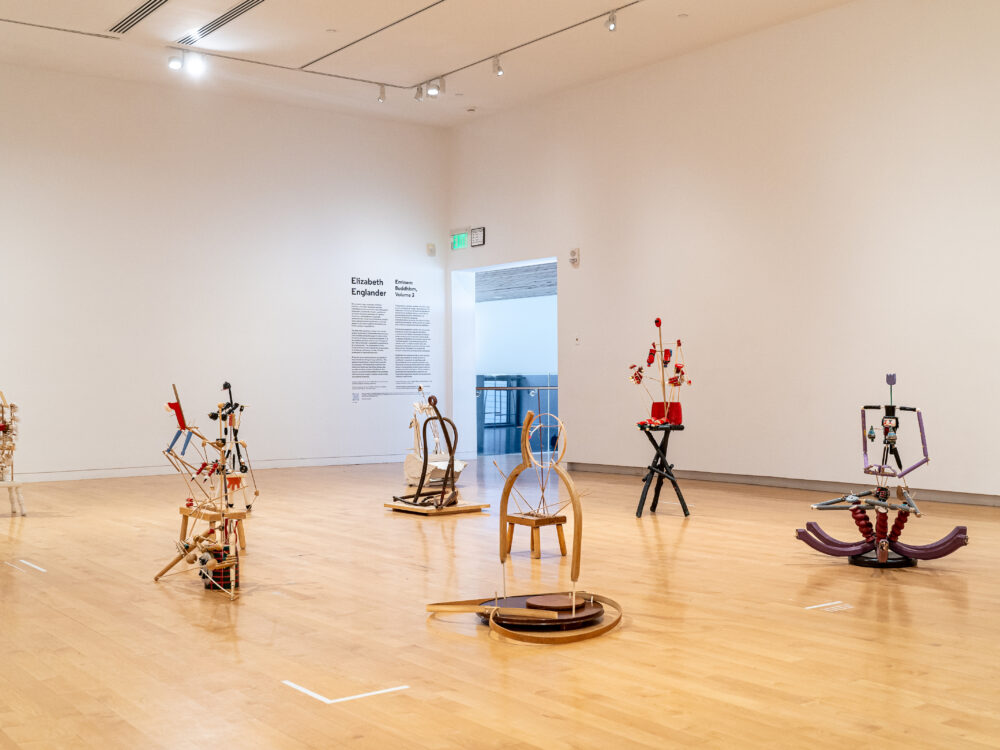 Seated figurative sculptures positioned on a floor in a gallery.